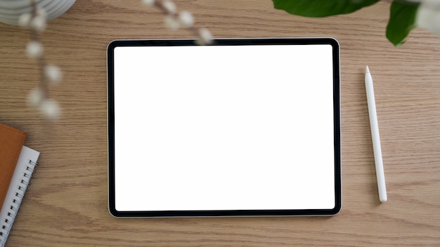 Vista superior do espaço de trabalho simples com tablet de tela em branco, caneta e caderno