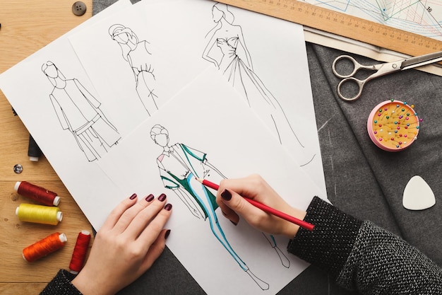 Foto vista superior do estilista no trabalho. mãos femininas desenhando roupas em seu espaço de trabalho criativo, vista superior