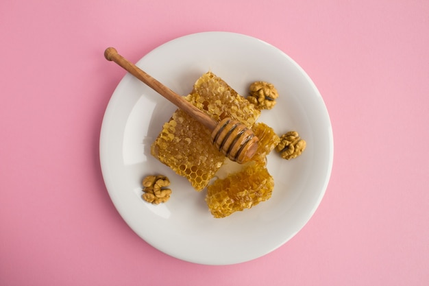 Vista superior do favo de mel e nozes no prato branco na mesa rosa