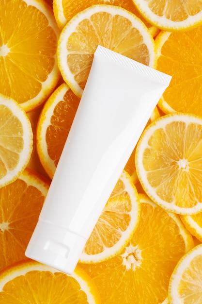 Vista superior do frasco sem marca para produtos cosméticos. Frasco plástico para creme, loção corporal ou produtos de higiene pessoal. Suculentas fatias de laranja e limão no fundo. Copie o espaço, plana lay. Conceito de cuidados com a pele e beleza