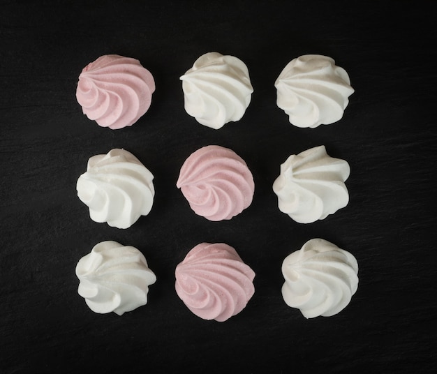 Vista superior do fundo da textura dos cookies de merengue branco e rosa. Padrão de merengues de whisk tradicional, creme para bater no forno em ardósia preta, maquete de beze plana