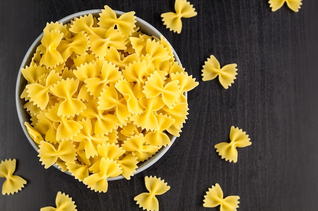 Vista superior do fundo preto com farfalle cru italiano ou macarrão em tigela com espaço de cópia