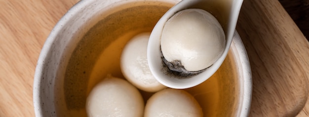 Vista superior do grande tangyuan de gergelim (tang yuan, bolas de bolinho de arroz glutinoso) com sopa de calda doce em uma tigela no fundo da mesa de madeira para comida do festival do solstício de inverno.