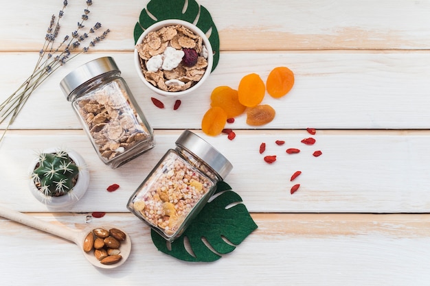 Vista superior do granola e cornflake jar perto de frutos secos e plantas suculentas em fundo de madeira