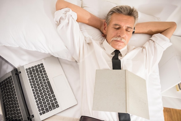 Vista superior do homem de negócios está dormindo de terno com notebook e laptop na cama no quarto de hotel