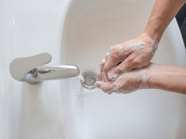 Vista superior do homem lavando as mãos com sabão antibacteriano sob torneira com água corrente