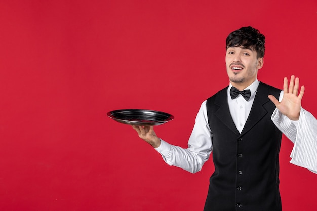 Vista superior do jovem curioso garçom de uniforme com gravata borboleta segurando a bandeja e uma toalha, mostrando cinco