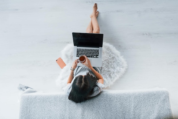 Vista superior do jovem em roupas casuais que sentado em casa sozinho com laptop e chá.