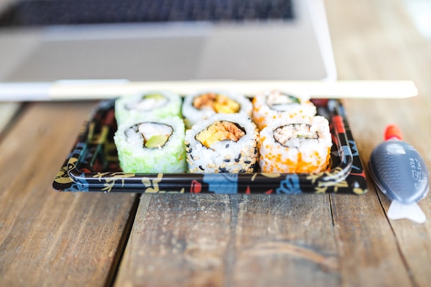 Foto vista superior do laptop e deliciosos rolos de sushi com vinho na mesa de madeira