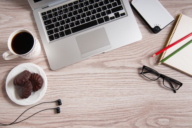 Vista superior do laptop e o bloco de notas com óculos e fones de ouvido na área de trabalho de madeira rústica e xícara de café.