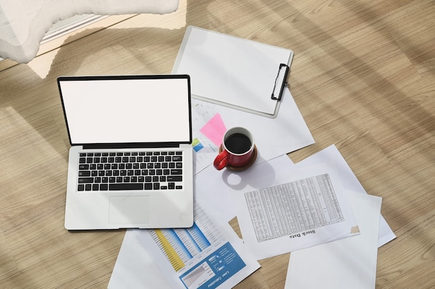 Vista superior do local de trabalho com a xícara de café, documento e laptop de tela em branco no piso de madeira.