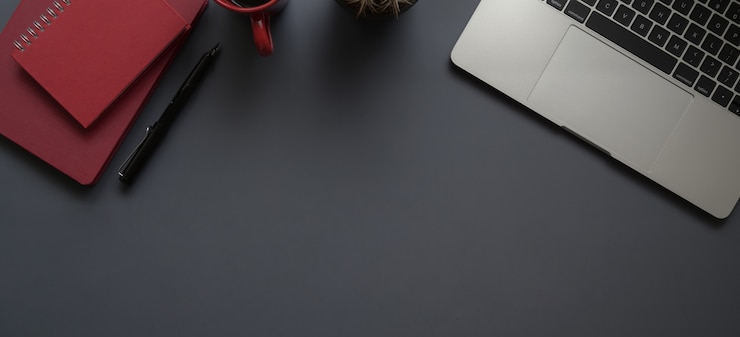 Foto vista superior do local de trabalho moderno escuro com computador portátil, material de escritório e caderno vermelho com espaço de cópia