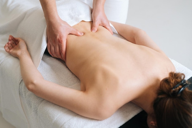 Vista superior do massagista masculino massageando a parte inferior das costas de uma jovem deitada na mesa de massagem no salão spa de luz Fisioterapeuta profissional realizando tratamentos de bem-estar para mulheres com dor nas costas