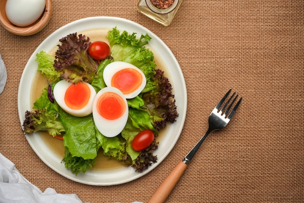 Vista superior do prato de salada com ovos cozidos, alface e tomate em jogo americano com garfo na mesa de jantar