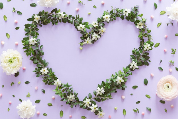 Vista superior do quadro de coração flor feito de flores silvestres, brotos e folhas em fundo lilás. Conceito de amor, plana leigos.