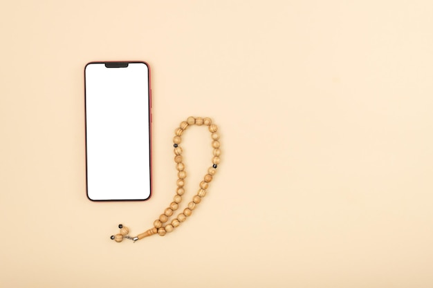 Vista superior do smartphone com tela branca ao lado de um rosário em uma maquete de fundo bege