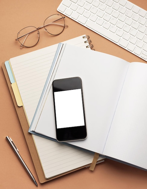 Foto vista superior do smartphone de material de escritório com tela de maquete em branco sobre óculos de canetas de notebooks