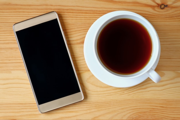 Vista superior do smartphone ouro com uma xícara de chá quente na mesa de madeira