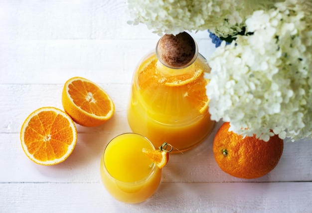 Vista superior do suco de laranja fresco em jarra e vidro com laranjas maduras na mesa de madeira branca no terraço de verão