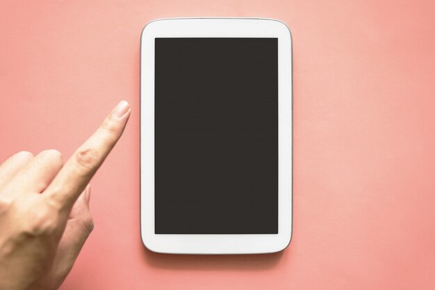 Vista superior do tablet de cor branca com tela preta e mão tocando no fundo da cor de papel rosa.