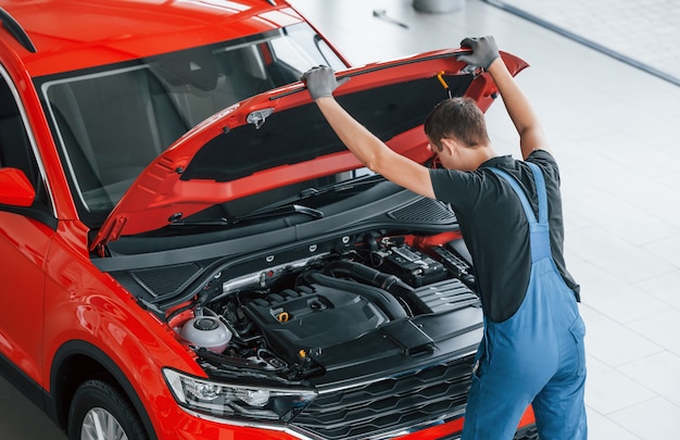 Foto vista superior do trabalhador masculino de uniforme que repara automóvel vermelho