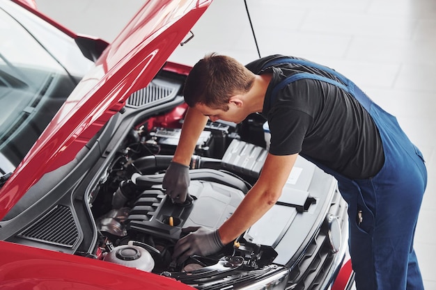 Foto vista superior do trabalhador masculino de uniforme que repara automóvel vermelho