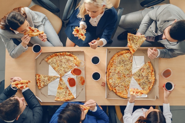 Vista superior dos empresários com roupa formal, sentado à mesa e comer pizza no almoço.