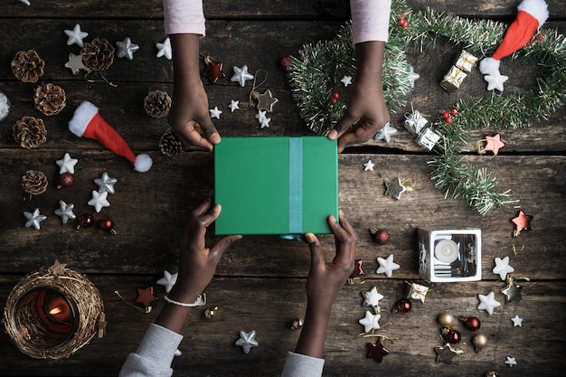 Vista superior de dos manos de niños de colores sosteniendo una caja de regalo de vacaciones de navidad verde