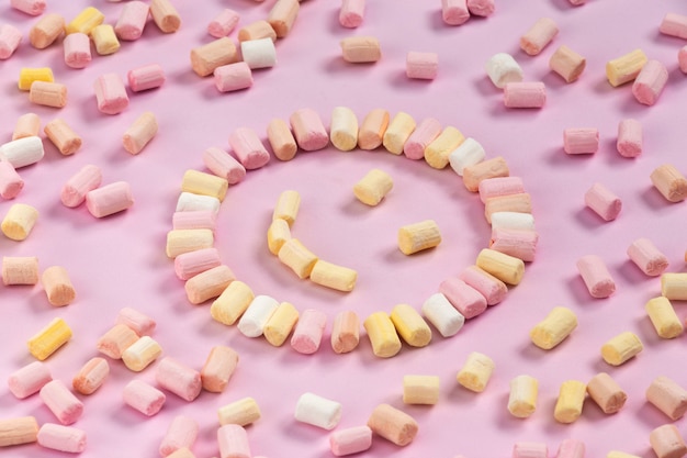 Vista superior dos marshmallows multi-coloridas que se encontra na forma de um smiley ou sol em um fundo rosa de uma cor