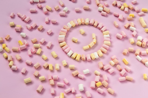 Vista superior dos marshmallows multi-coloridas que se encontra na forma de um smiley ou sol em um fundo rosa de uma cor