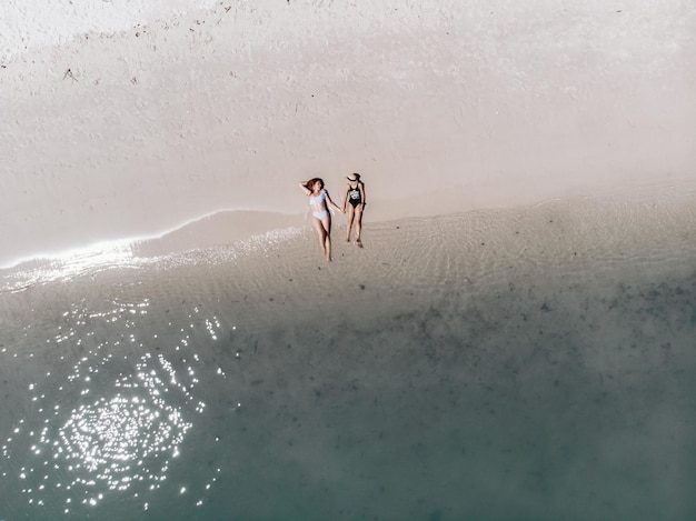 Vista superior de dos mejores amigos en traje de baño tomando el sol en la playa con rayos de sol y tomados de la mano en señal de su amistad. Concepto de amigos.