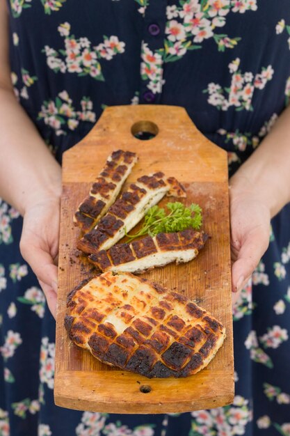 Vista superior de dos rebanadas a la parrilla de queso halloumi casero en borad de madera en manos de mujer