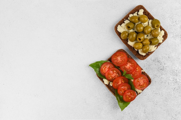 Vista superior de dos sándwiches abiertos con queso feta, tomate con albahaca y aceitunas sobre fondo de piedra clara con espacio de copia