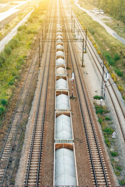 Vista superior dos trilhos da ferrovia com vagões com pedra em dia de verão