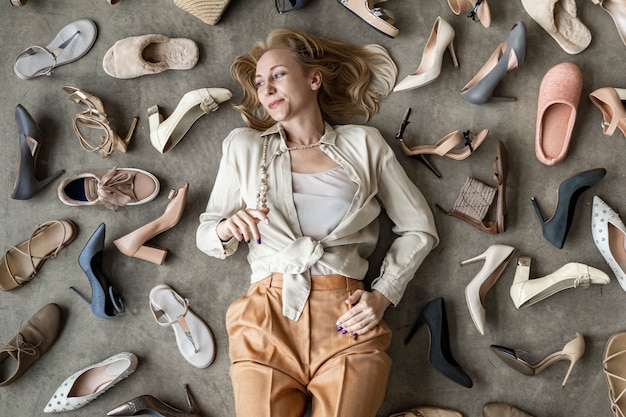 Foto vista superior elegante loira feminina posando escolhendo sapatos sentado no chão, vista de cima, muitos sapatos femininos ...