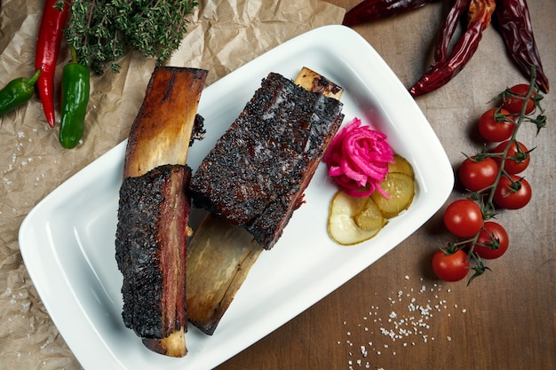 Vista superior em deliciosas costelas de carne defumadas e grelhadas apetitosas. Costelas de churrasco - um prato clássico da cozinha americana em um prato branco. mesa de madeira