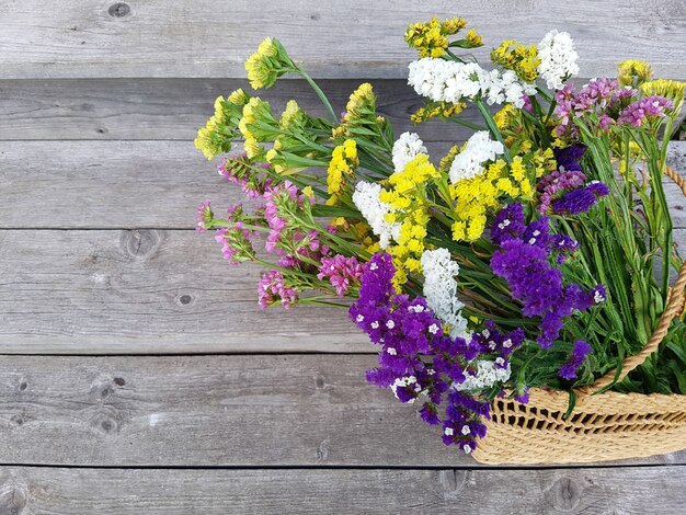 Vista superior em um buquê de flores em uma bolsa feminina de palha em um fundo de tábuas de madeira