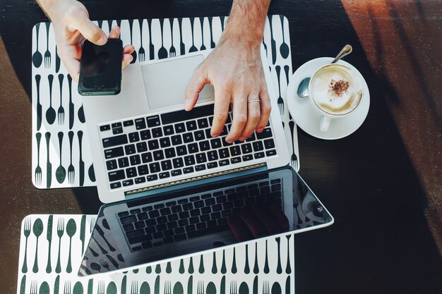 Vista superior del empresario usando una computadora portátil y un teléfono inteligente mientras trabaja en un café