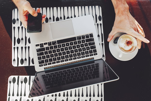 Vista superior del empresario usando una computadora portátil y un teléfono inteligente mientras trabajaba en la cafetería, recortada