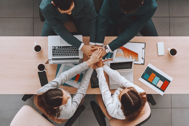 Vista superior de empresarios en ropa formal apilando las manos sobre la mesa.