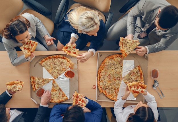 Vista superior de empresarios en ropa formal sentado a la mesa y comer pizza para el almuerzo.