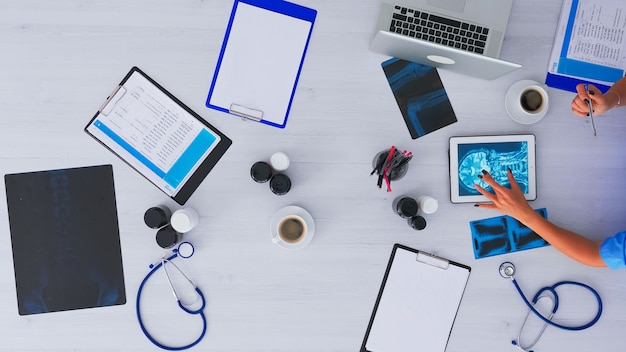 Vista superior de la enfermera analizando el cerebro humano usando tableta en flatlay sentado en el escritorio en la clínica con rayos X y dispositivos digitales