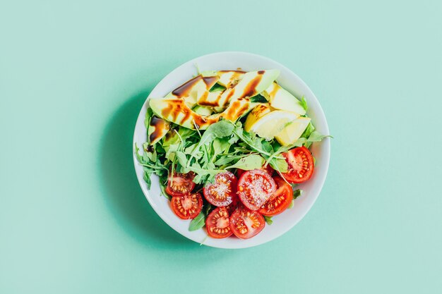 Vista superior de ensalada de tomate rúcula aguacate limón en plato blanco sobre fondo verde