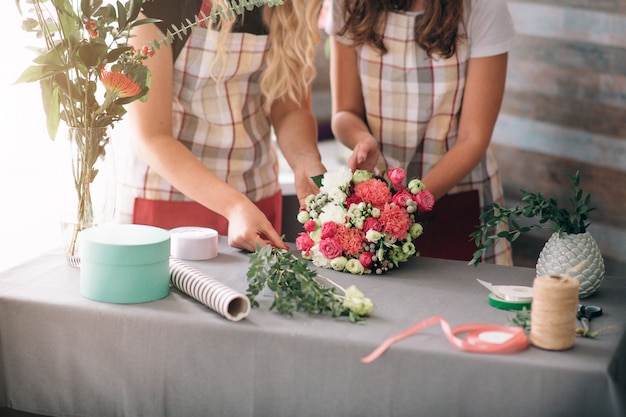 Foto vista superior de la entrega de flores. floristas creando orden, haciendo ramo de rosas en florería. dos floristas están haciendo ramos de flores. una mujer recogiendo rosas para un ramo, otra niña también está trabajando.