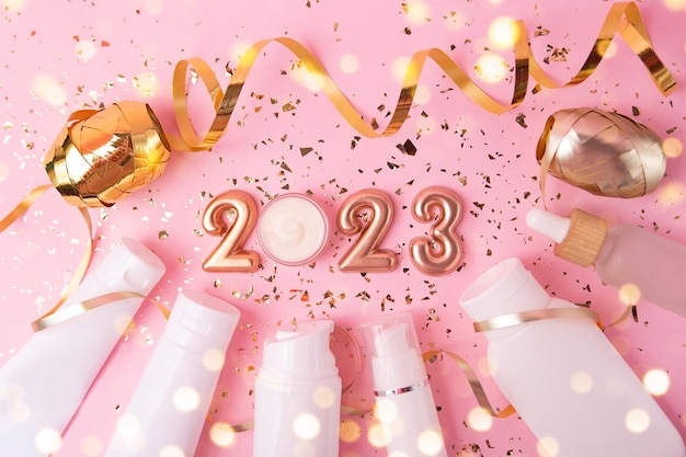 Vista superior de los envases de cosméticos sobre fondo rosa Números de oro rosa 2023 arriba