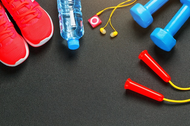 Vista superior de equipo deportivo, mancuernas, una cuerda para saltar, una botella de agua, zapatillas y un jugador.