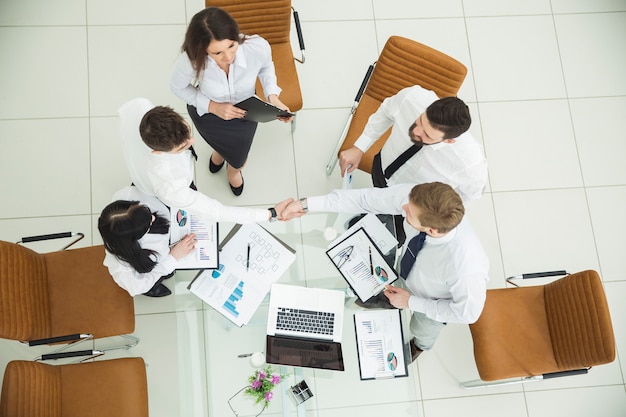 Vista superior: equipo de negocios exitoso dándose la mano con nuevos socios comerciales después de la conclusión del contrato financiero en la sala de conferencias.La foto tiene un espacio vacío para su texto.