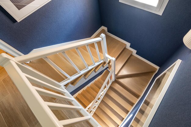 Vista superior de una escalera de caracol brillante con escalones de parquet de madera pulida y barandillas blancas mate