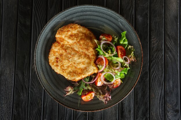 Vista superior de escalope en empanado con verduras frescas y aros de cebolla roja