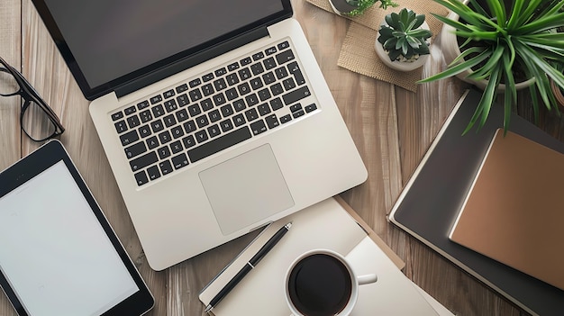 Vista superior de un escritorio de madera con una computadora portátil, tabletas, cuadernos, pluma, taza de café y plantas